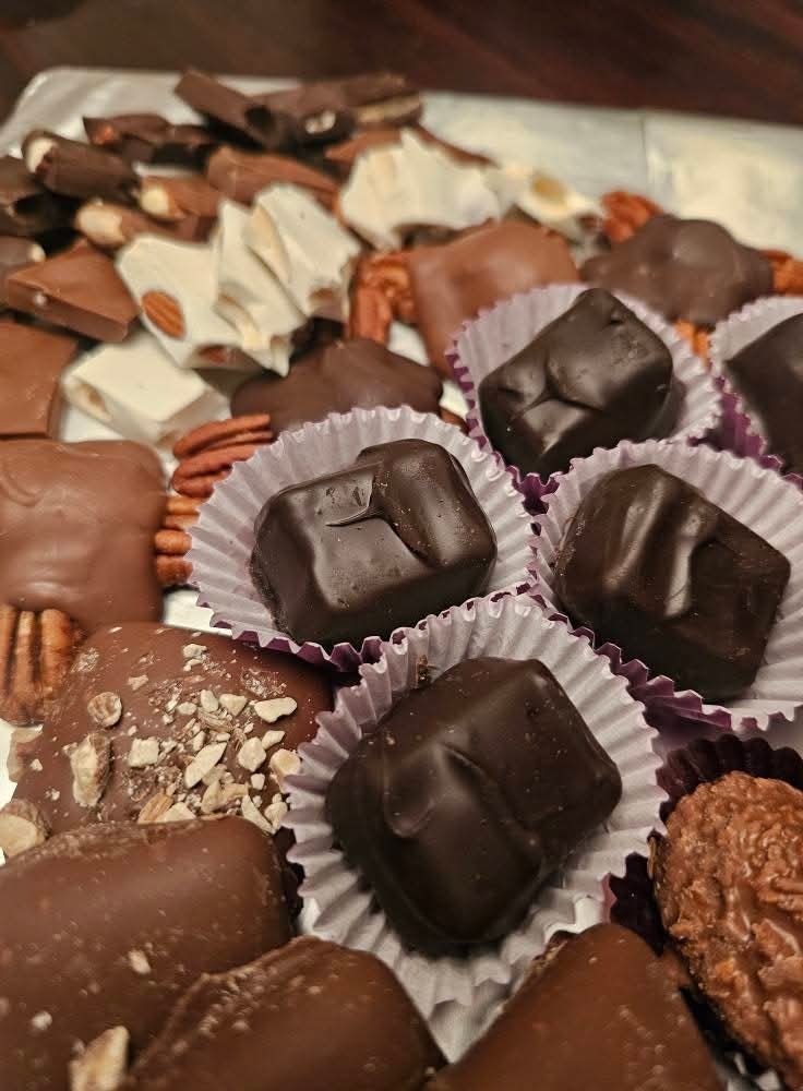 Assorted chocolates and pralines arranged on a tray with nuts and paper cups.