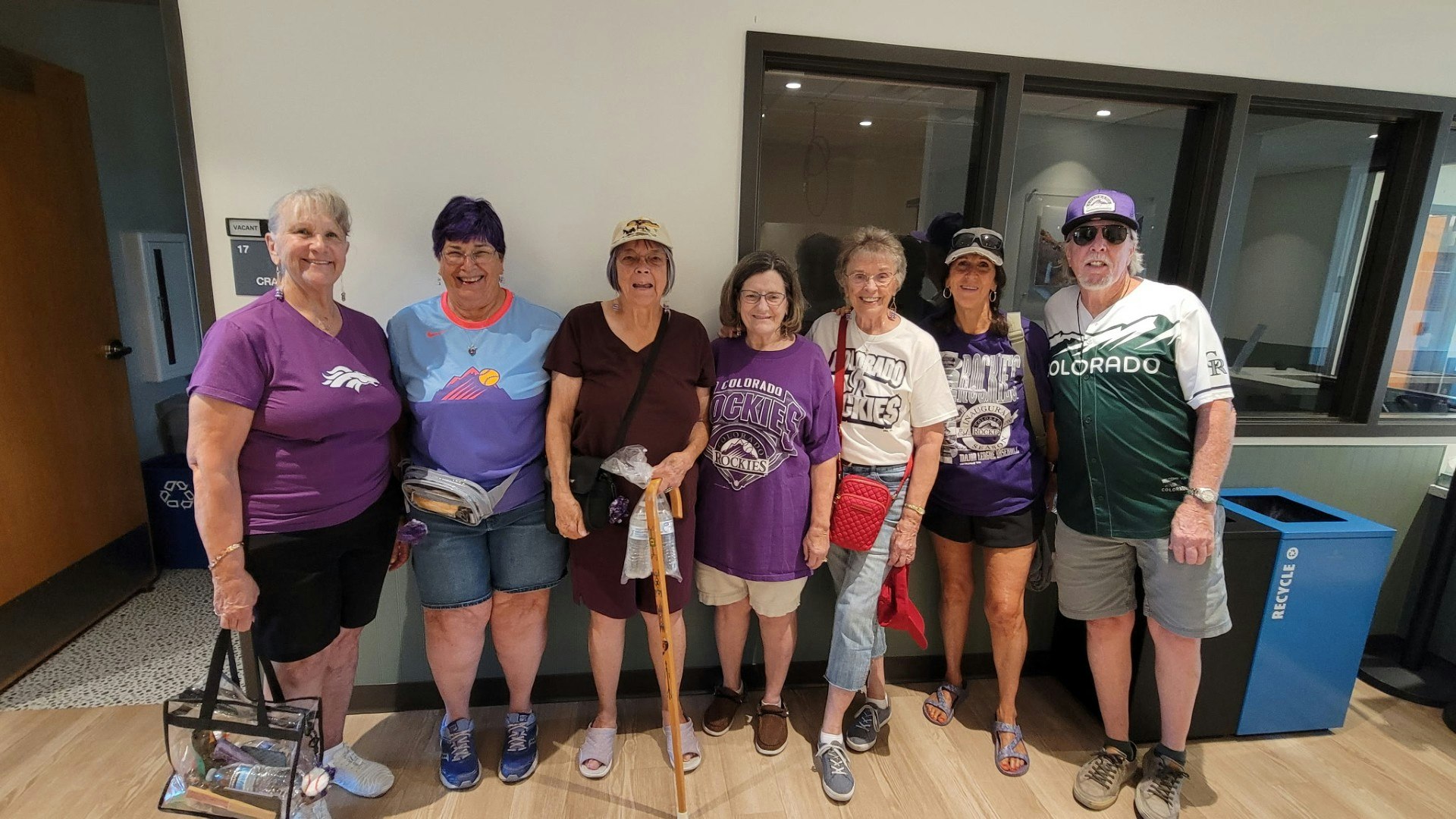 A group of eight people, mostly women, wearing team shirts and casual attire, gathered in a communal space.