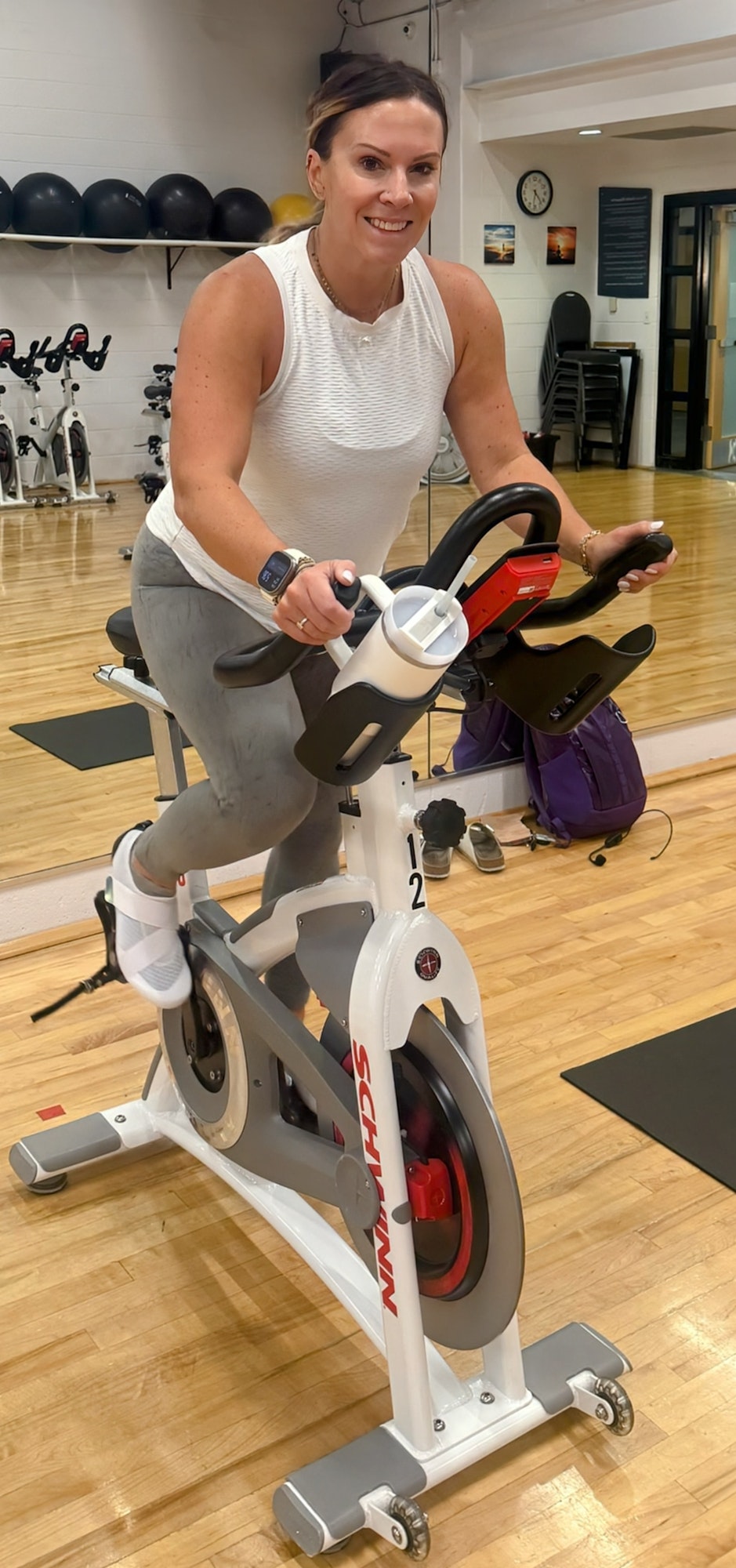 A person cycling on a stationary bike at a gym, smiling, wearing workout clothes.