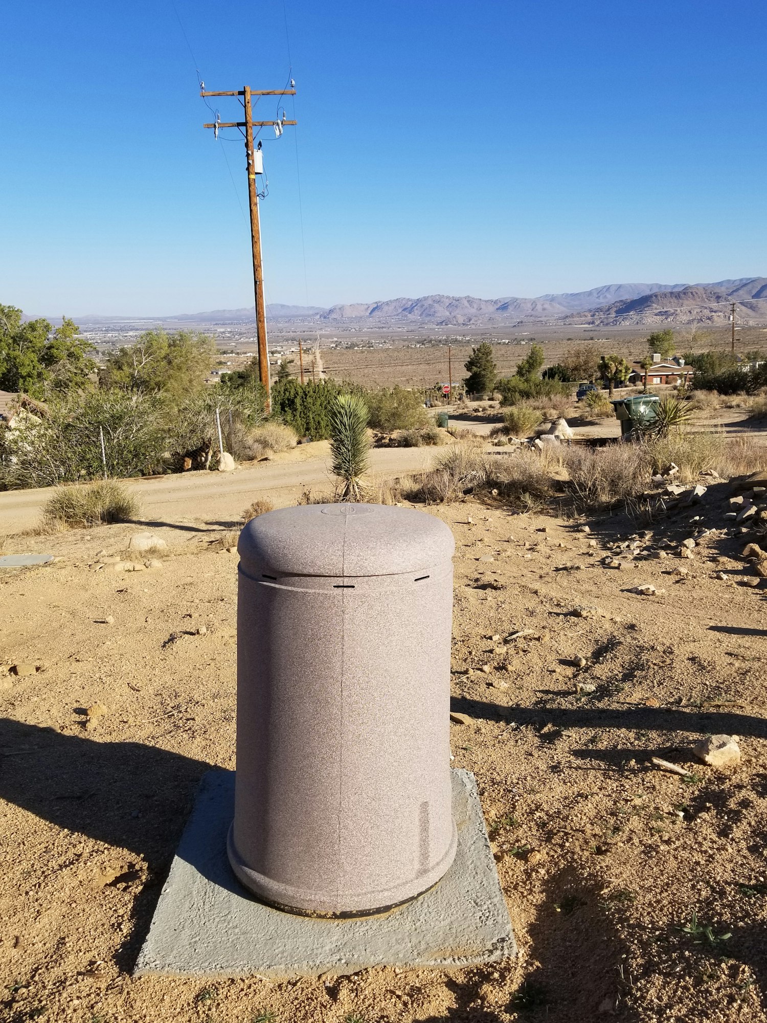 Desert landscape with a utility pole, mountains in the distance, and a large cylindrical object in the foreground.