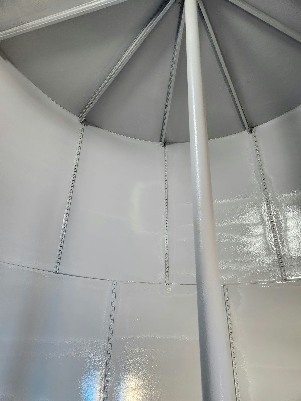 Interior of a structured canopy or tent with fabric panels and seams converging on a central pole.