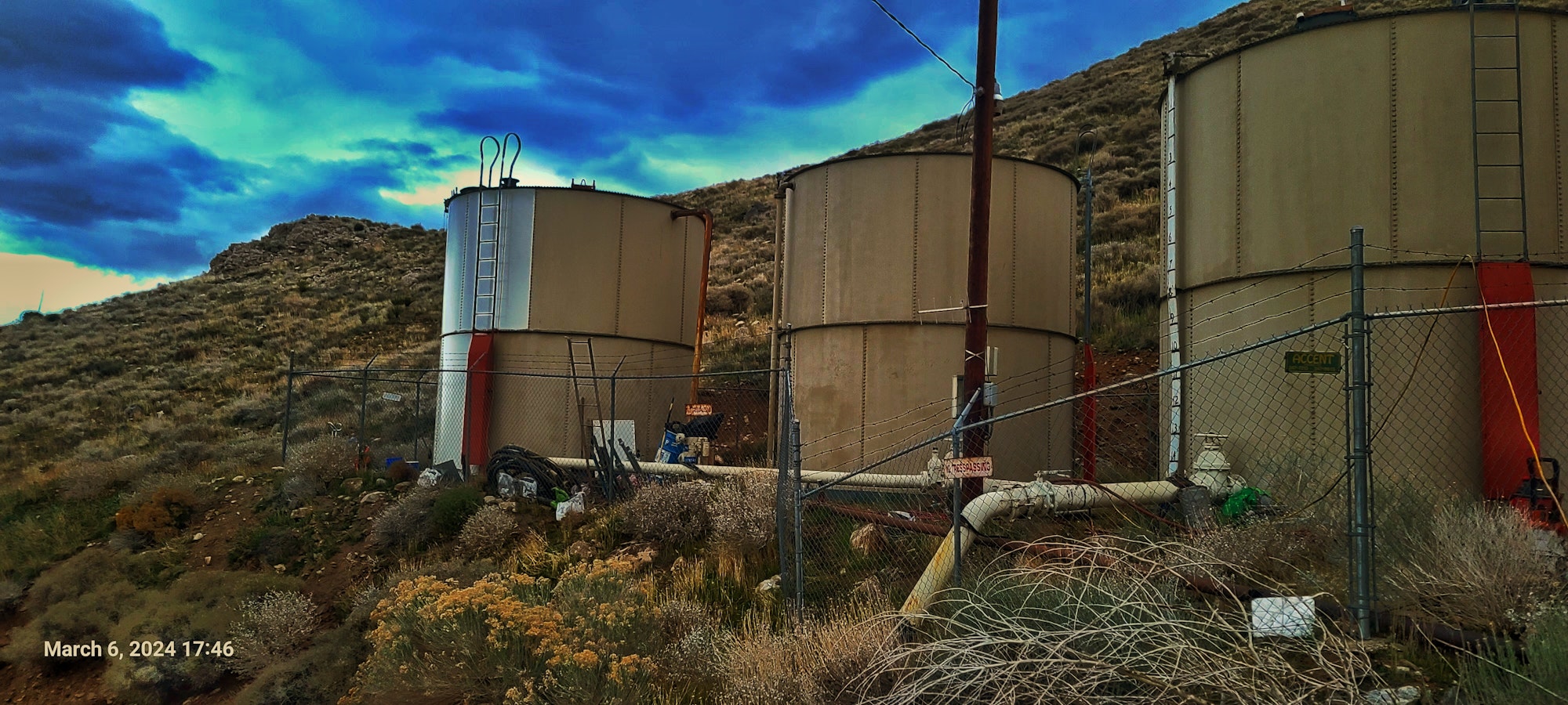 Three large industrial tanks behind a fenced area and cloudy skies in the background.