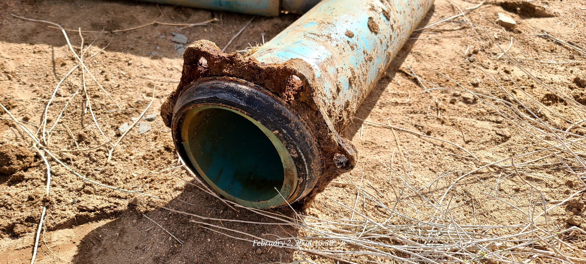 A corroded blue water pipe laying on sandy ground with visible interior.