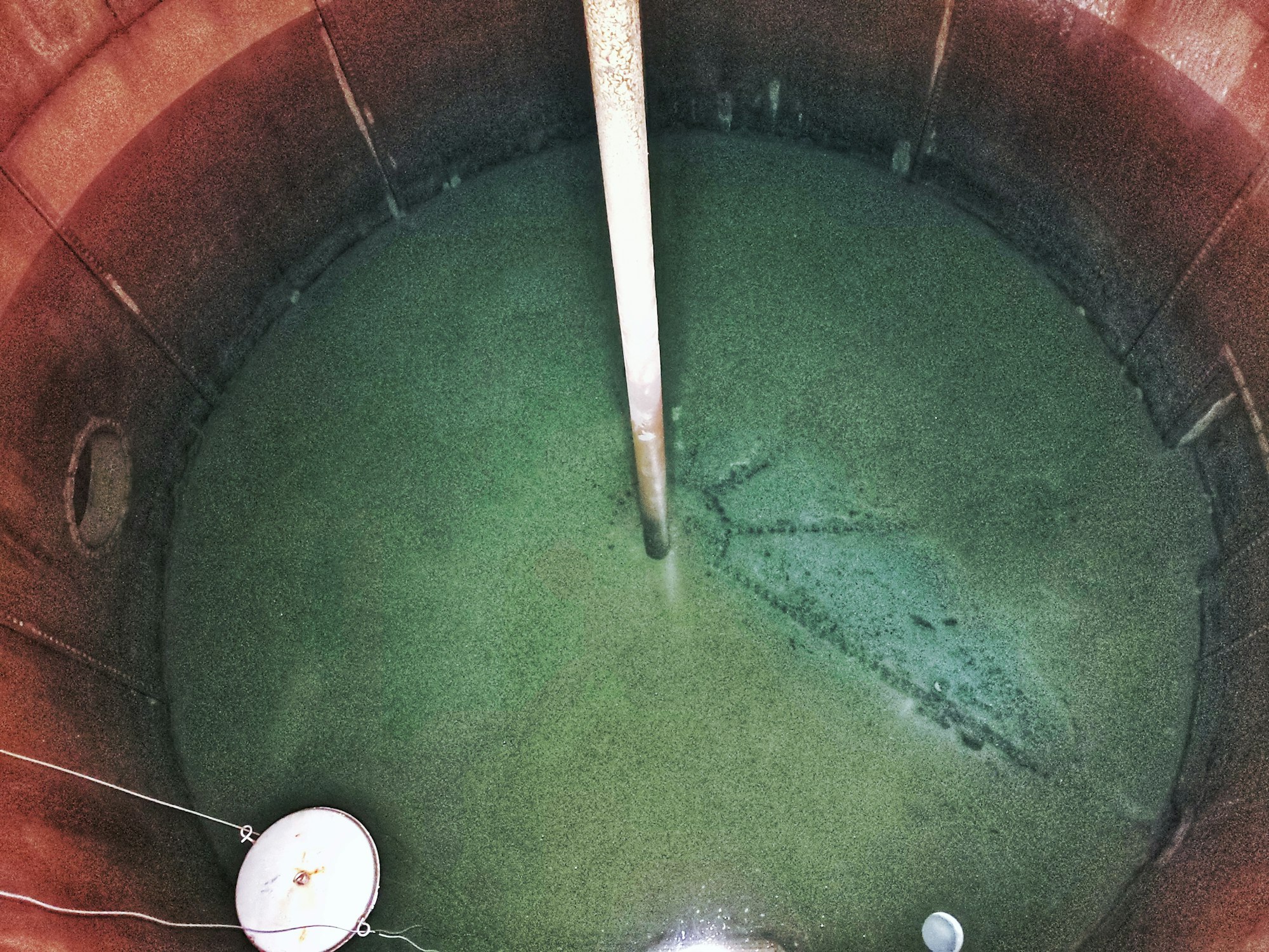 An overhead view of a large water tank filled with water.  Showing corrosion