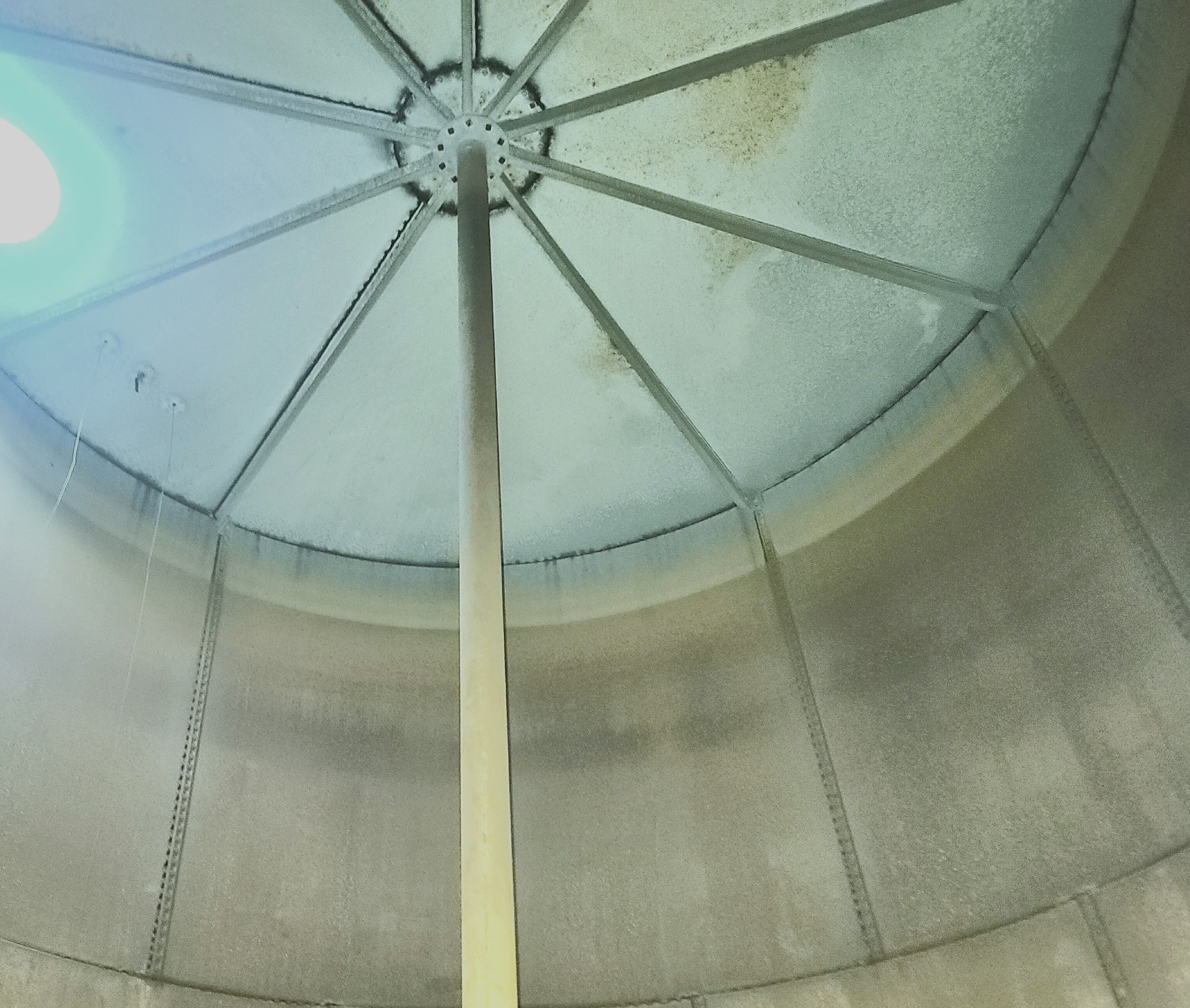 Interior of a water storage tank with a central beam and a domed ceiling, showing signs of corrosion.
