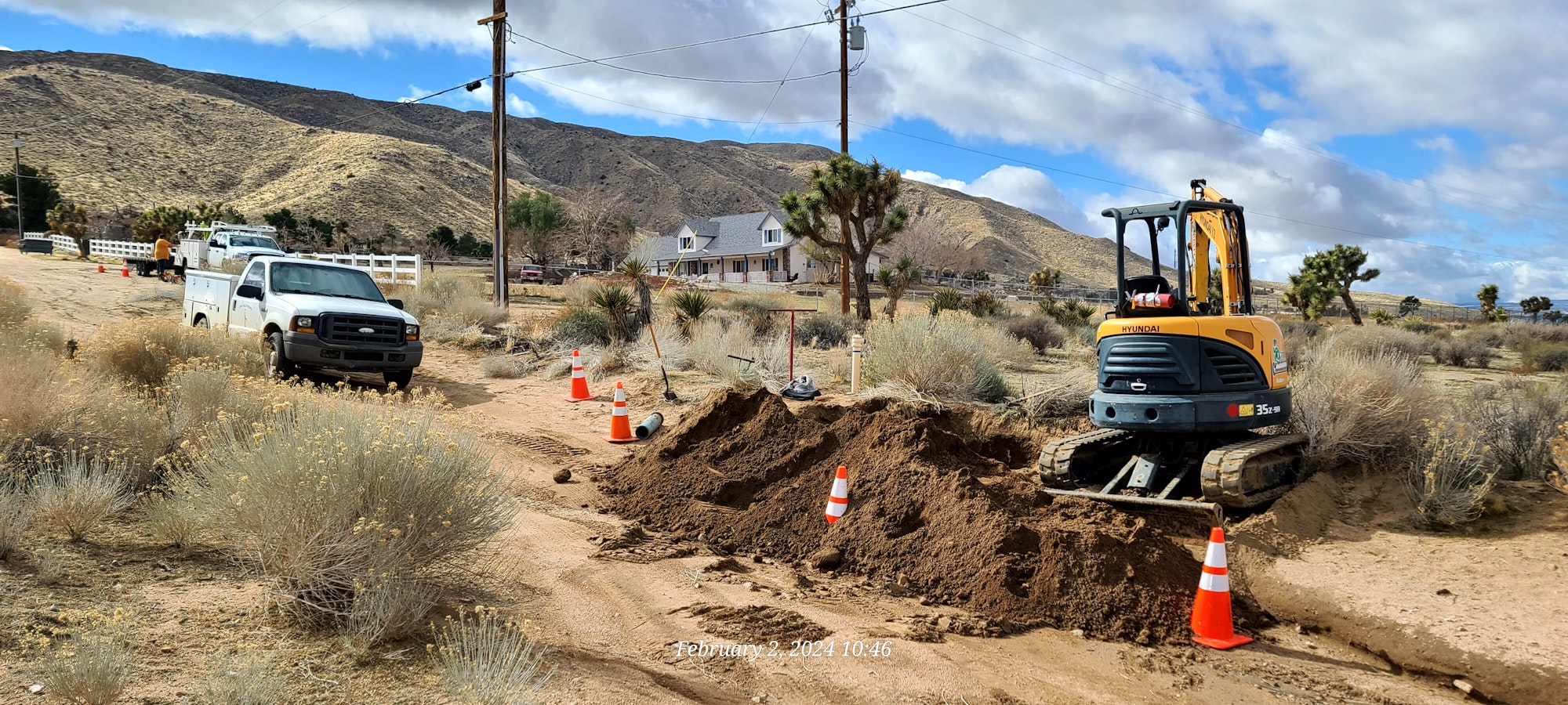 Construction equipment and vehicles at a desert work site, with safety cones and a trench.
