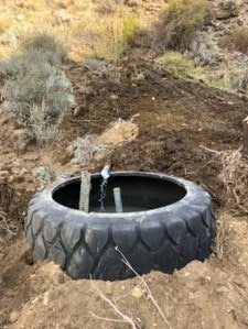 An excavated area featuring a large tire, possibly used for water collection or as a storage container in a rural setting.