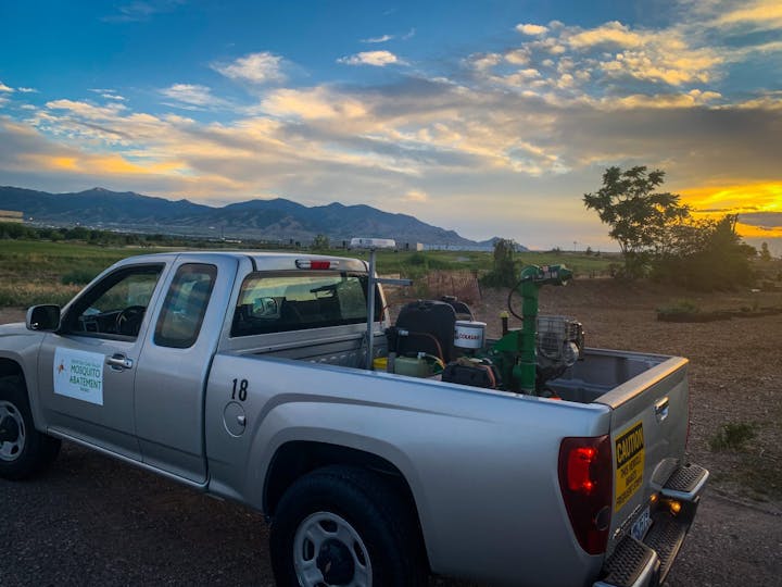 A pickup truck with mosquito control equipment, at sunset with mountains in the background.