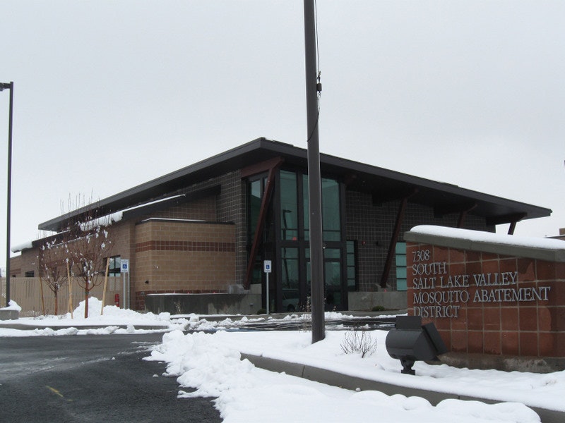 A modern building with a sign for the Salt Lake Valley Mosquito Abatement District, surrounded by snow.