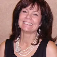 The image shows a woman with dark hair, wearing a black dress and pearl jewelry, smiling warmly at the camera.