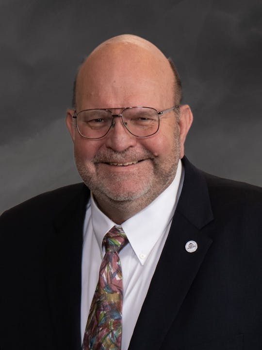 A smiling man in a suit and colorful tie, wearing glasses.