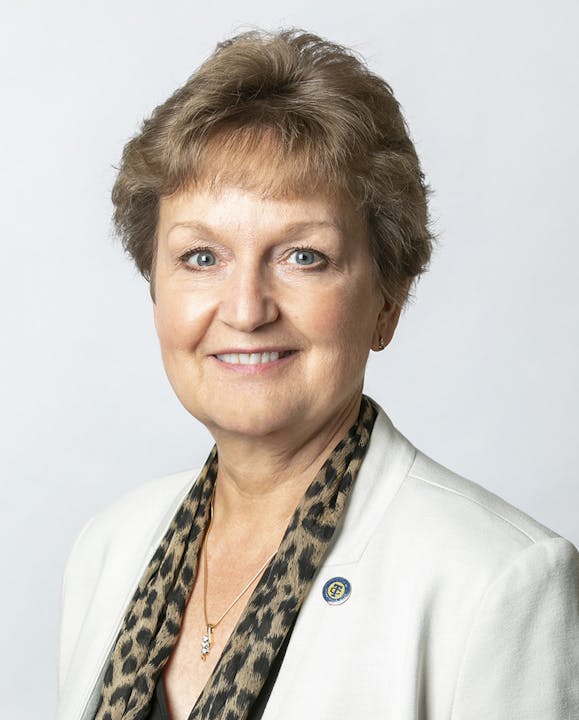 A person wearing a white blazer and a leopard print scarf, smiling.
