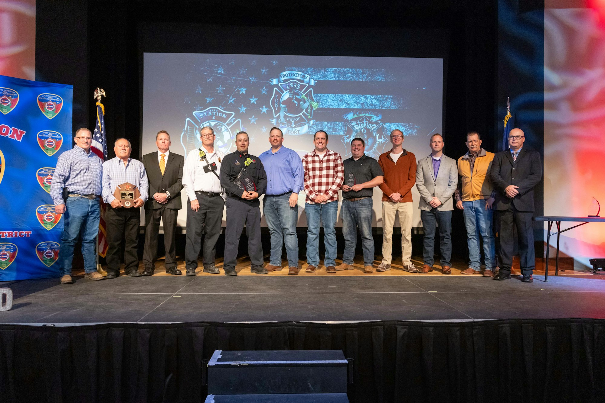 A group of men standing on a stage at an awards ceremony with a fire station theme in the background.
