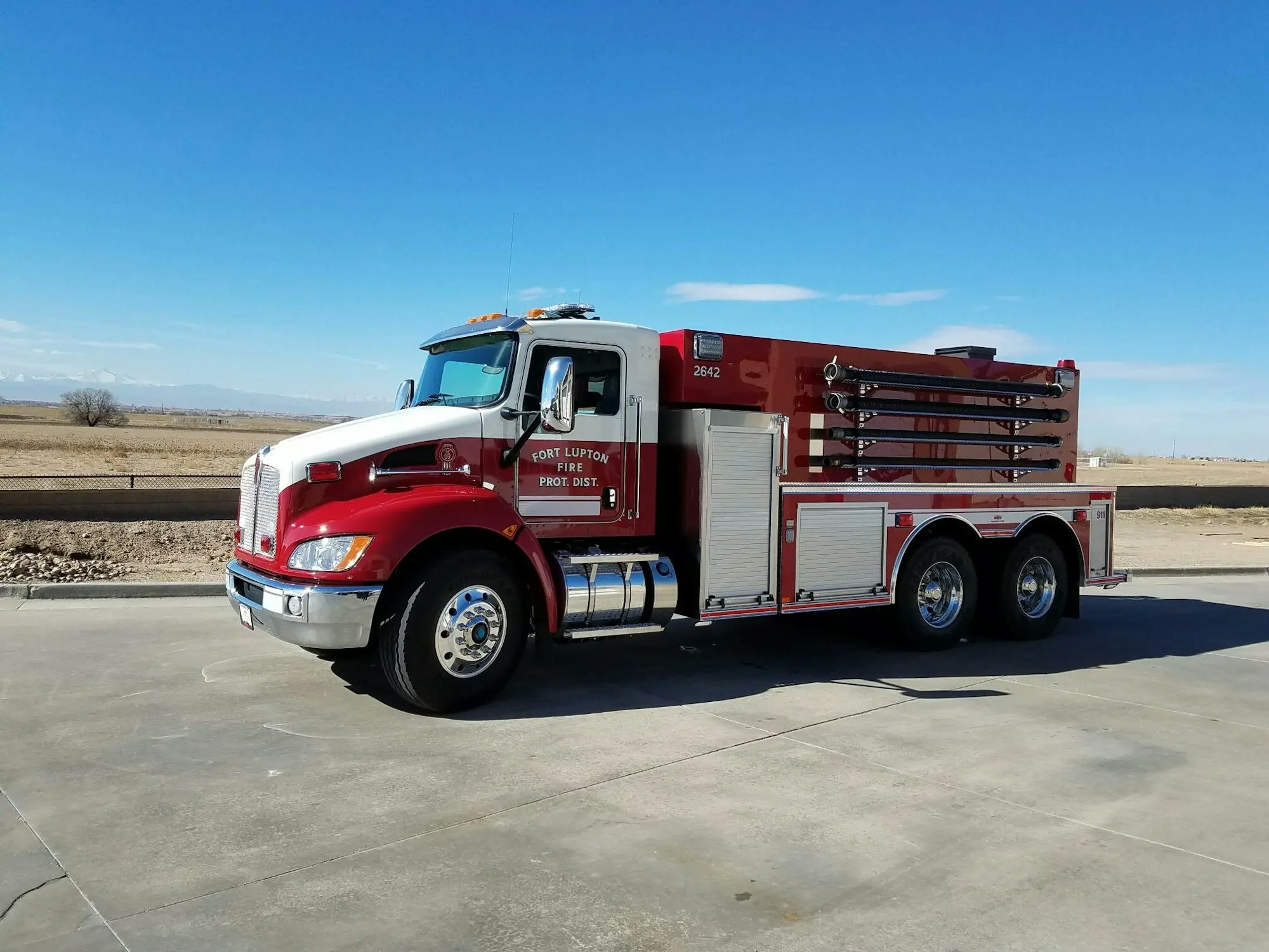 A red fire truck parked on concrete with a clear sky and distant mountains in the background.
