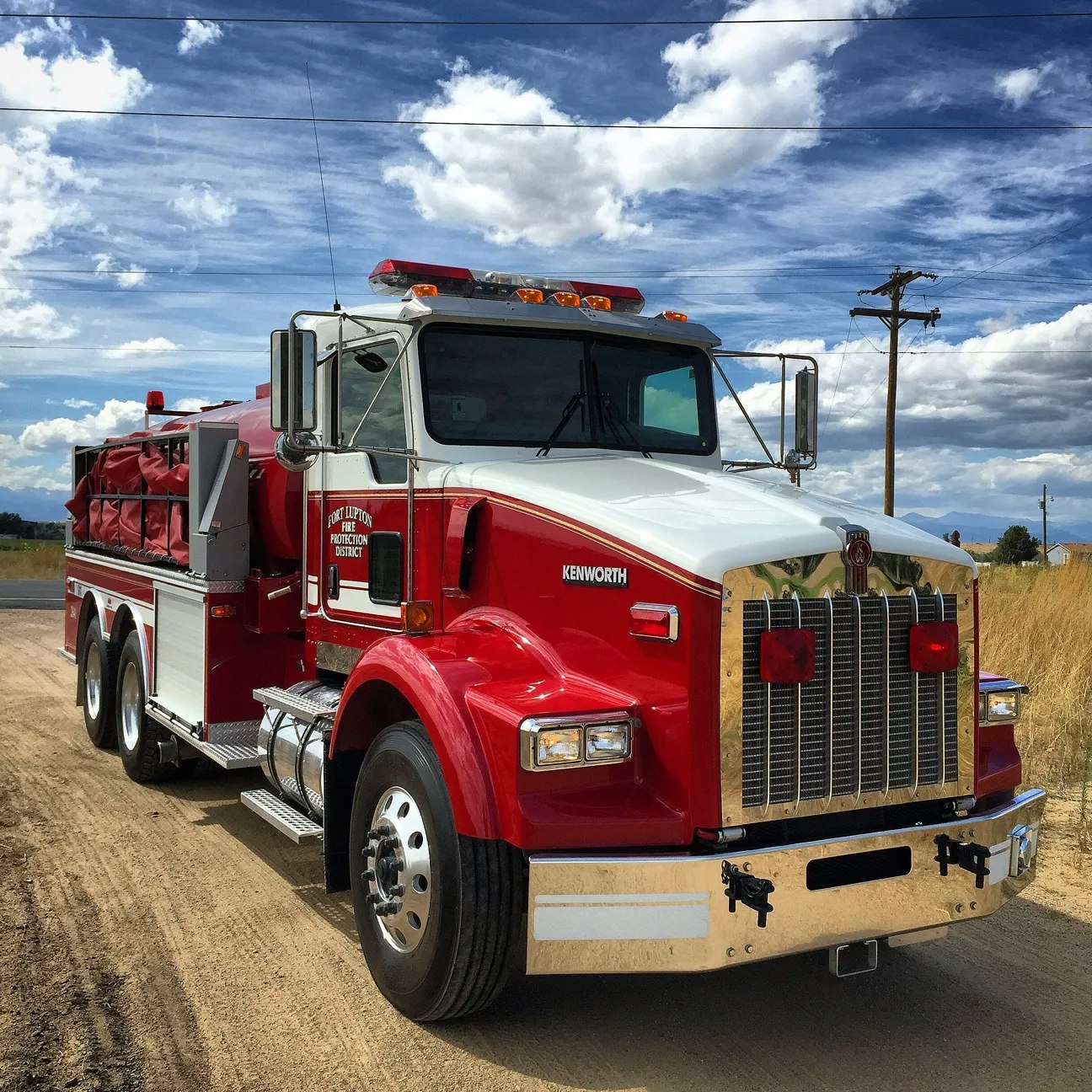 A red Kenworth fire truck on a road under a cloudy sky.