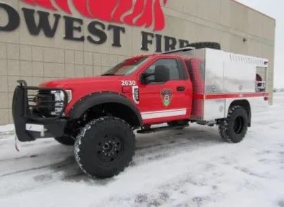 Red fire service pickup truck equipped for rugged terrain, parked on snow-covered ground.