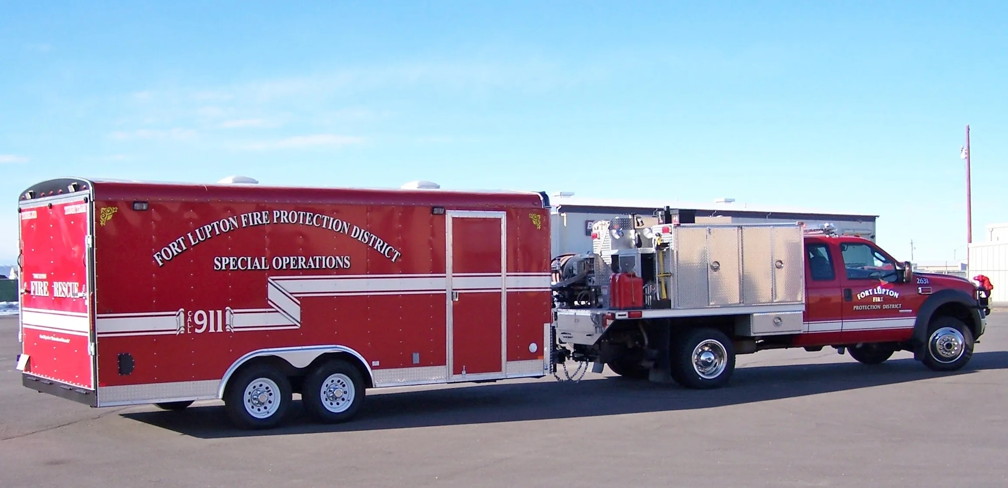 A red fire department specialized operations trailer and truck parked on a concrete surface under a clear sky.