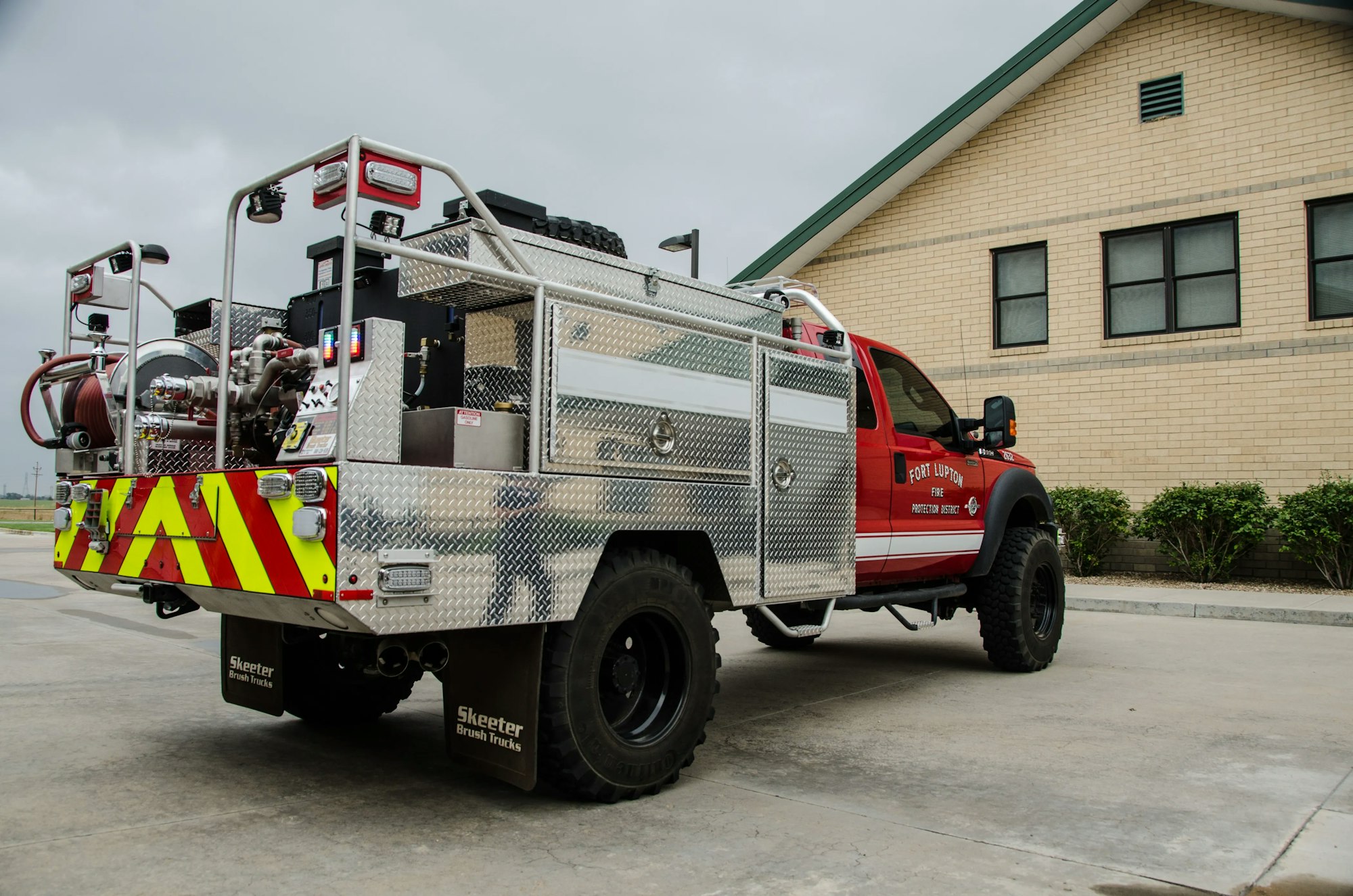 A red fire department brush truck with equipment parked outside a building.