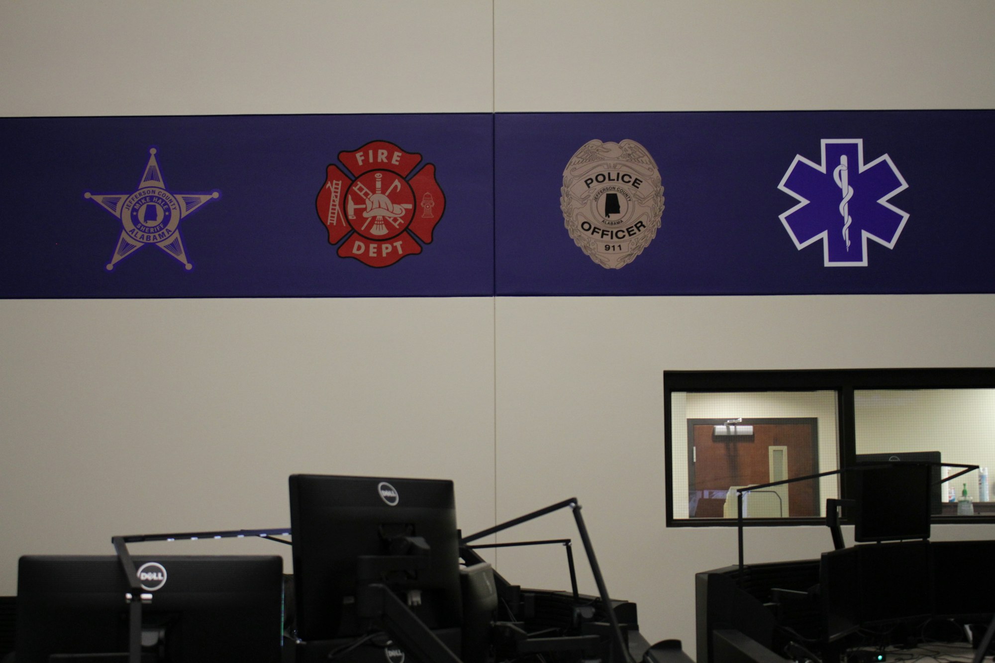 Wall with emblems of police, fire department, and medical services above office desks.