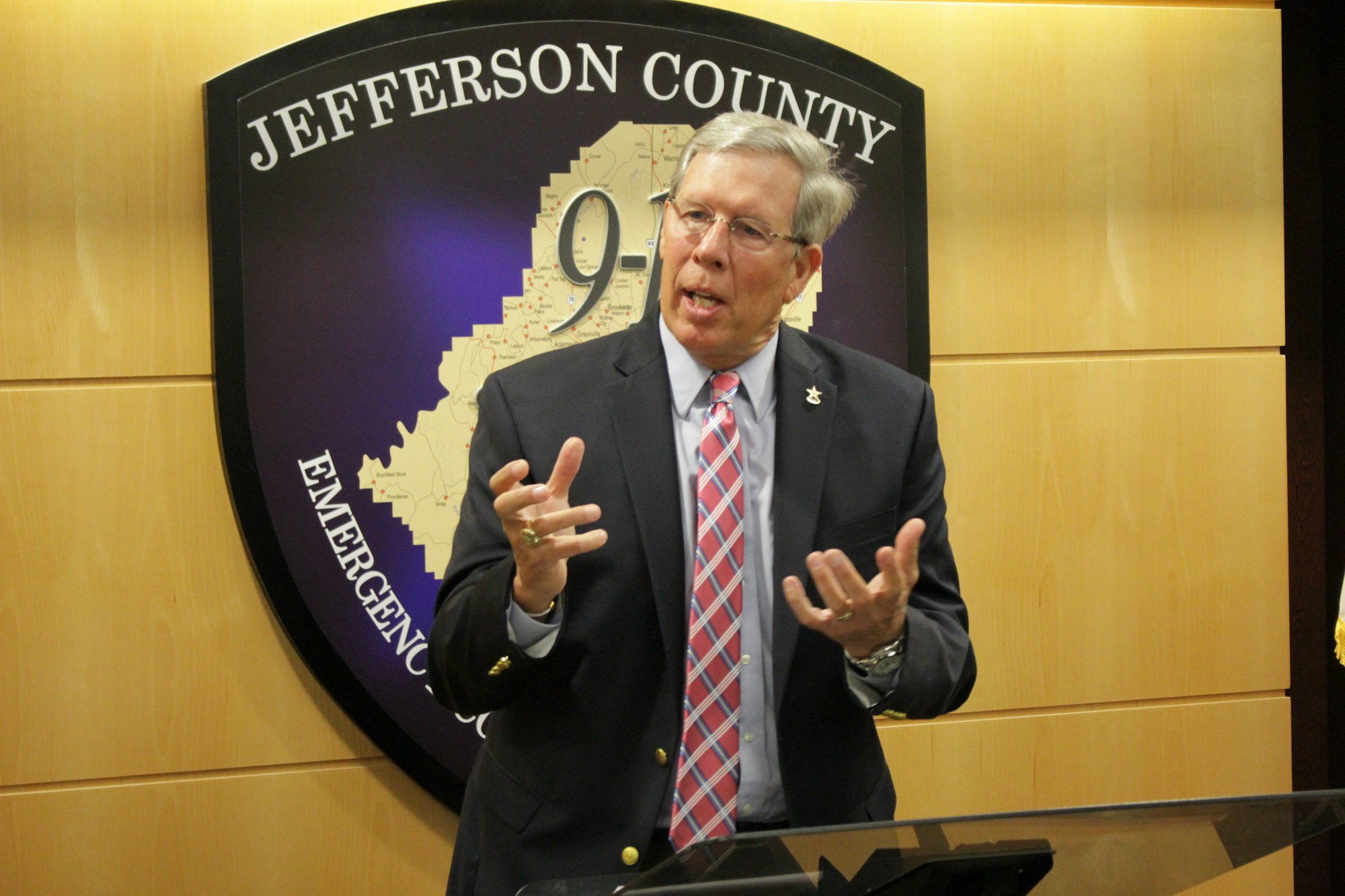 A man speaking at a podium with a "Jefferson County Emergency" sign in the background.