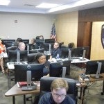 People working at computer stations in an office with an American flag.