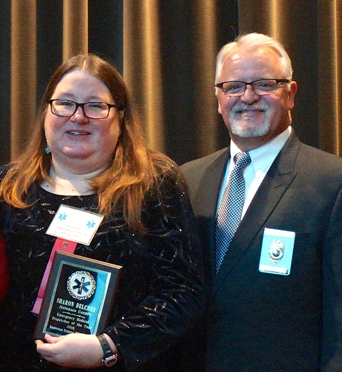 Two people pose for a photo; one holds a plaque.