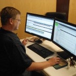 A person is using a computer with dual monitors displaying detailed information on a desk.