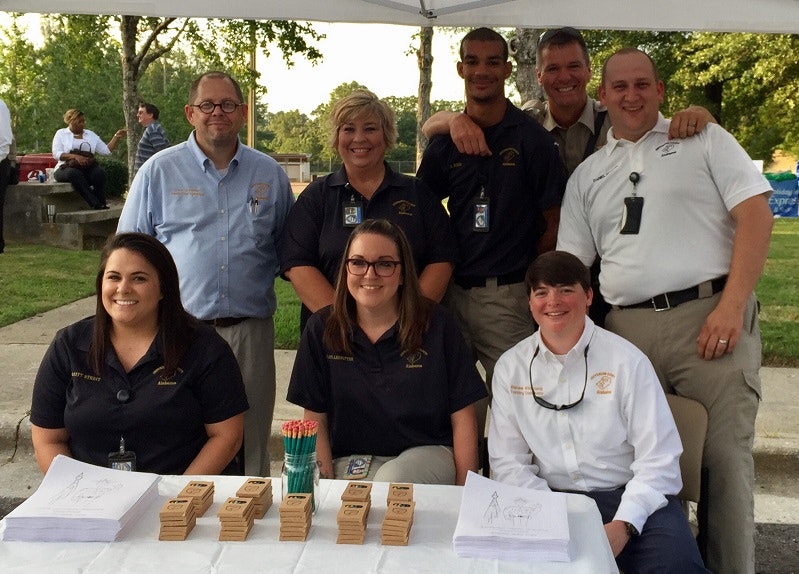 A group of people smiling at a table with papers and wooden blocks, outdoors under a canopy.