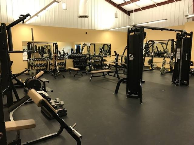 A gym with various exercise equipment, including weights, benches, machines, and mirrors on the walls.