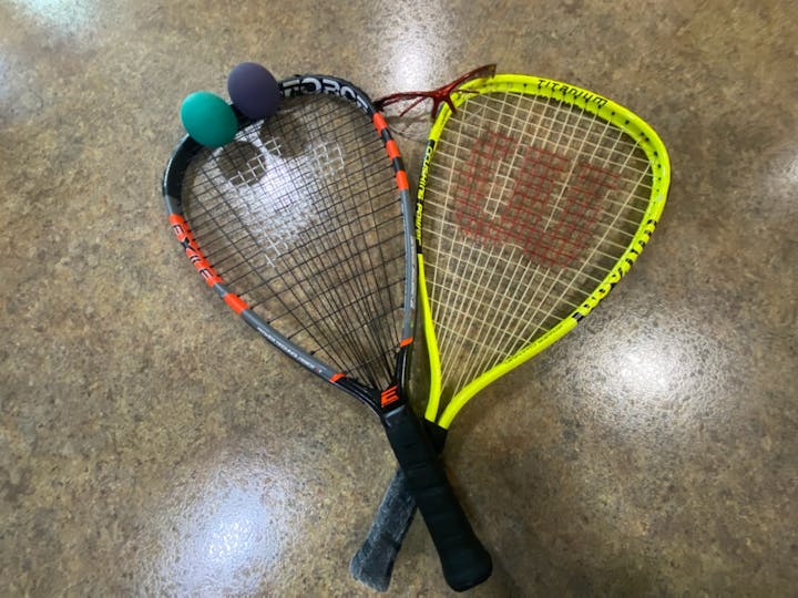Two racquets and two squash balls on a wooden floor.