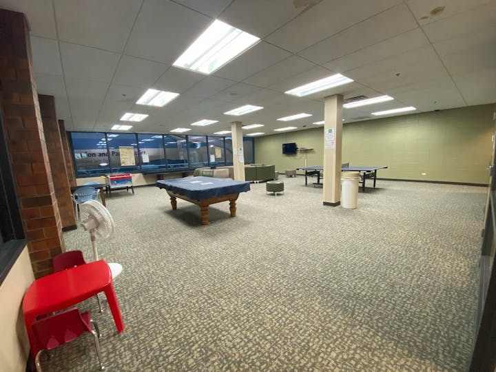 A recreation room with a pool table, table tennis, foosball, chairs, and tables.
