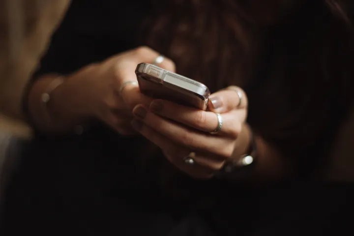 A person is holding a smartphone, with rings adorning their fingers, focusing on the device.