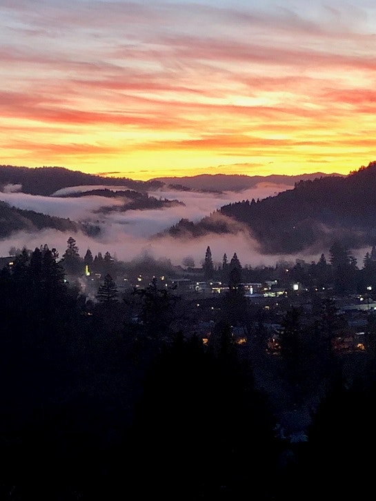 photo of Garberville at sunset with fog rolling into the river valley and town lights blinking through the trees