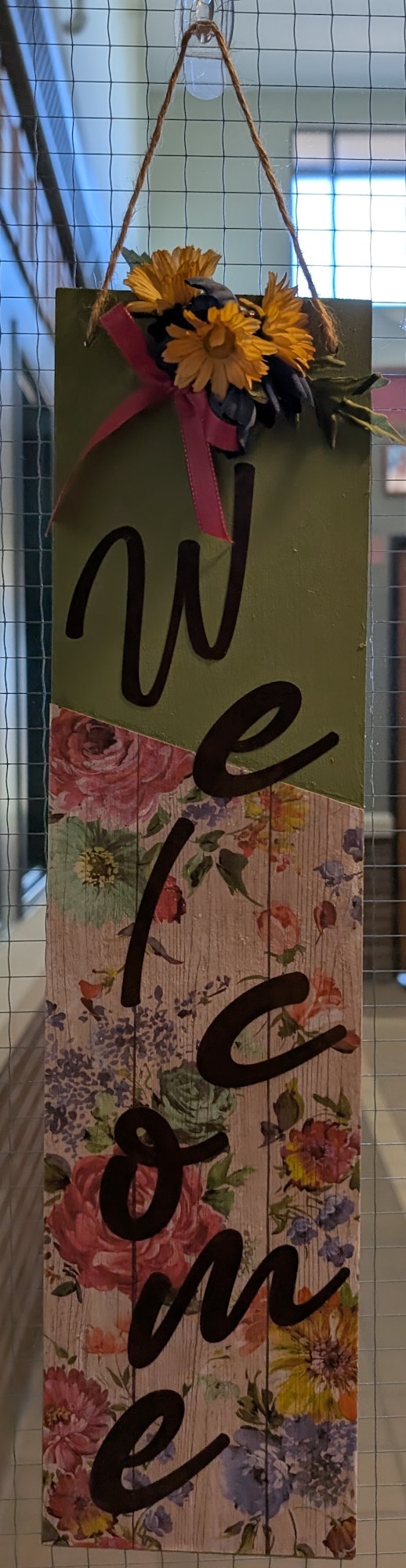 A hanging floral "Welcome" sign with sunflowers and colorful, floral patterns.