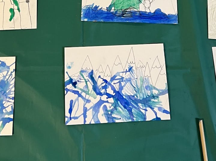 The image shows a colorful child’s drawing of mountains with blue and green abstract lines representing water or waves.