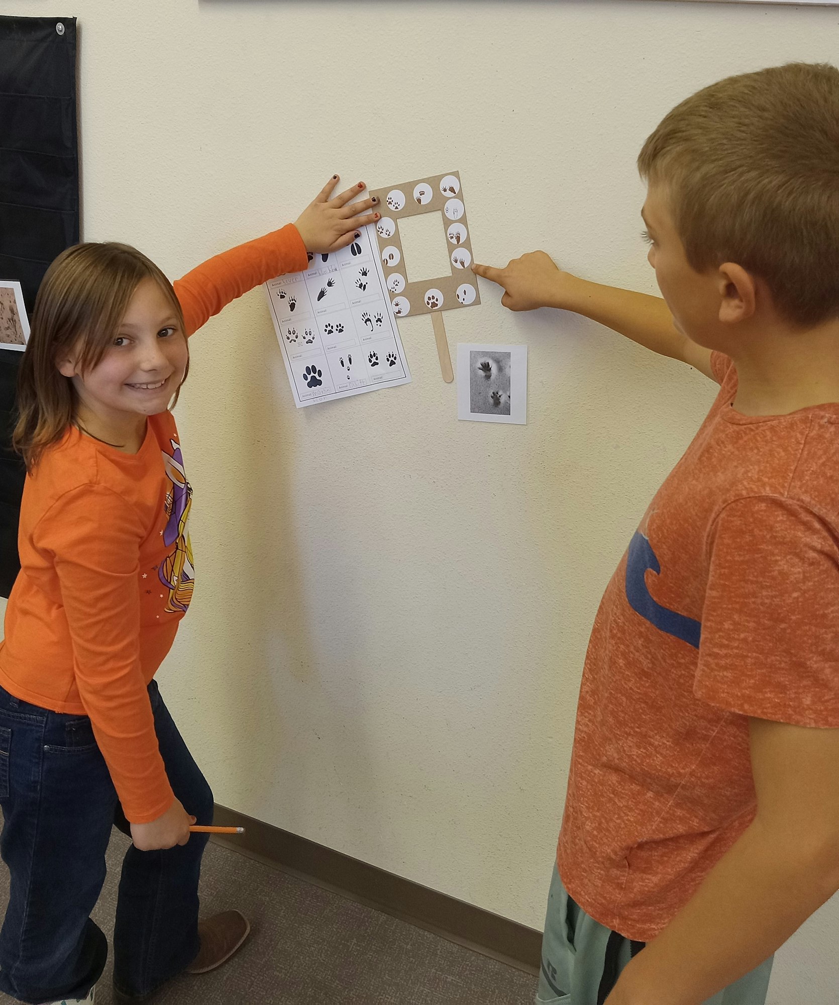 Two kids playing an educational matching game with animal cards on a wall.