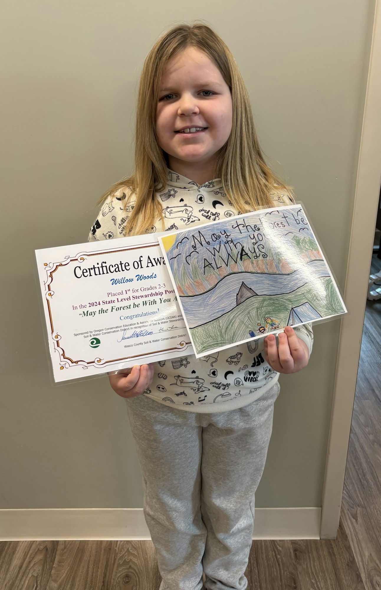 A child holding a Certificate of Award and a drawing with the text "May the forest be with you always."