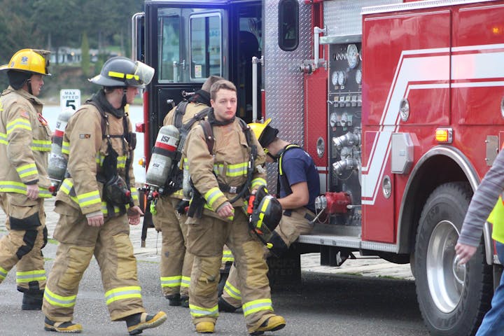 Firefighters in gear are near a fire truck, preparing for action or responding to an incident.