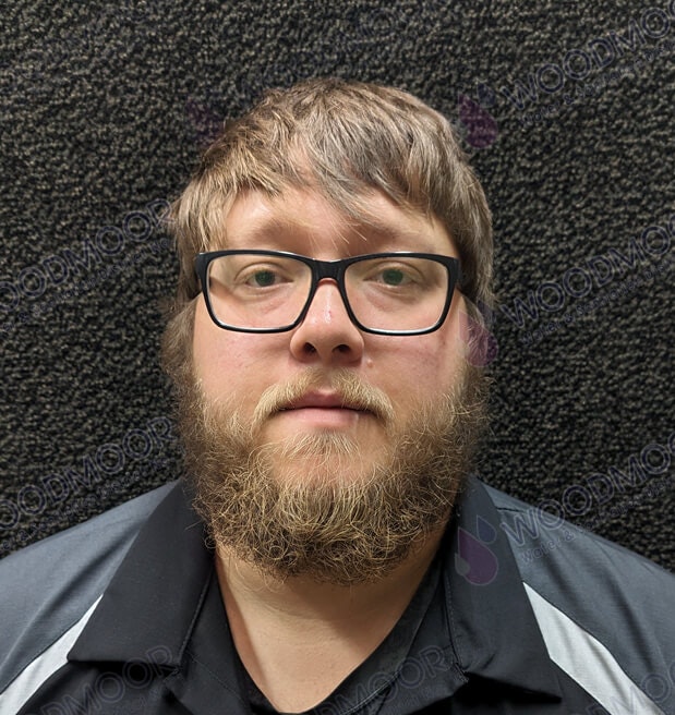 A person with glasses and a beard, wearing a collared shirt, against a textured background with "WOODMOOR" watermark.