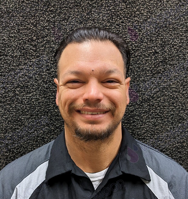 A smiling person with short hair and a goatee wearing a dark collared shirt. The background is black with a rough texture.