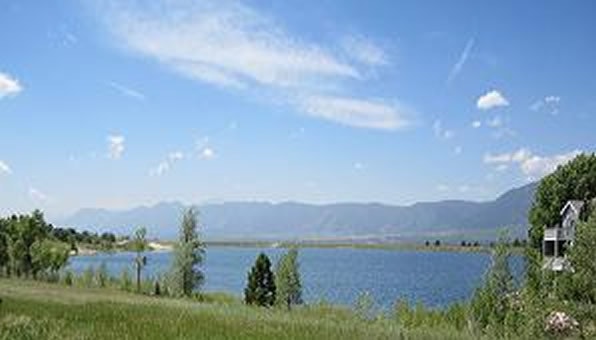 A lake surrounded by greenery, with mountains in the background under a blue sky with clouds.