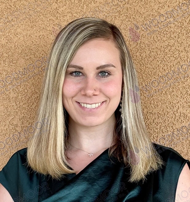 A person with shoulder-length blonde hair smiling in front of a textured wall.