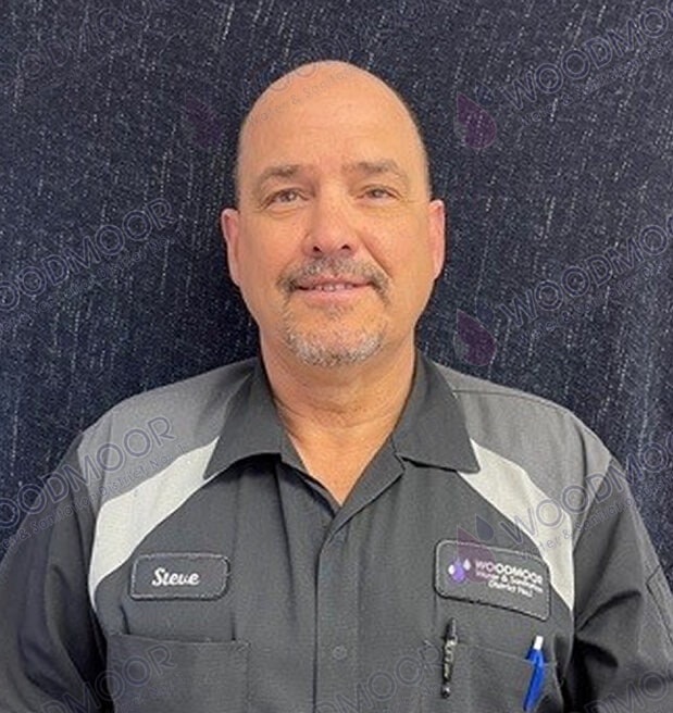 A person in a work uniform with name tags stands against a dark textured background.