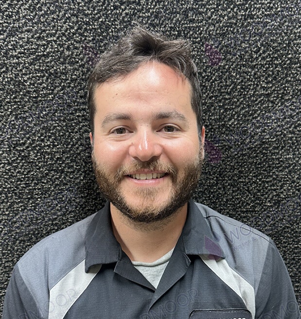 A man with a beard, smiling, wearing a collared shirt in front of a textured wall.