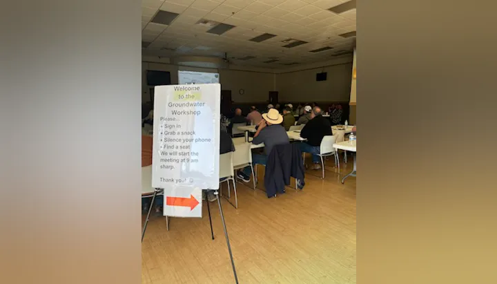 A Groundwater Workshop in a communal space with attendees seated, focusing on sign-in and meeting instructions.