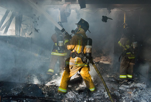 Firefighters battling a smoky blaze indoors, using hoses and wearing protective gear.