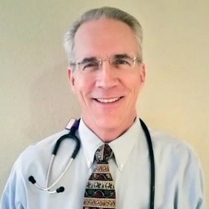 A smiling man in a dress shirt and tie, wearing glasses, with a stethoscope around his neck.