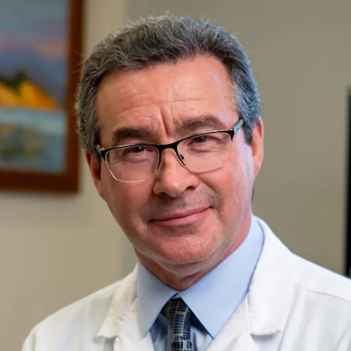 The image shows a man wearing glasses and a white lab coat, appearing professional, likely in a healthcare setting.
