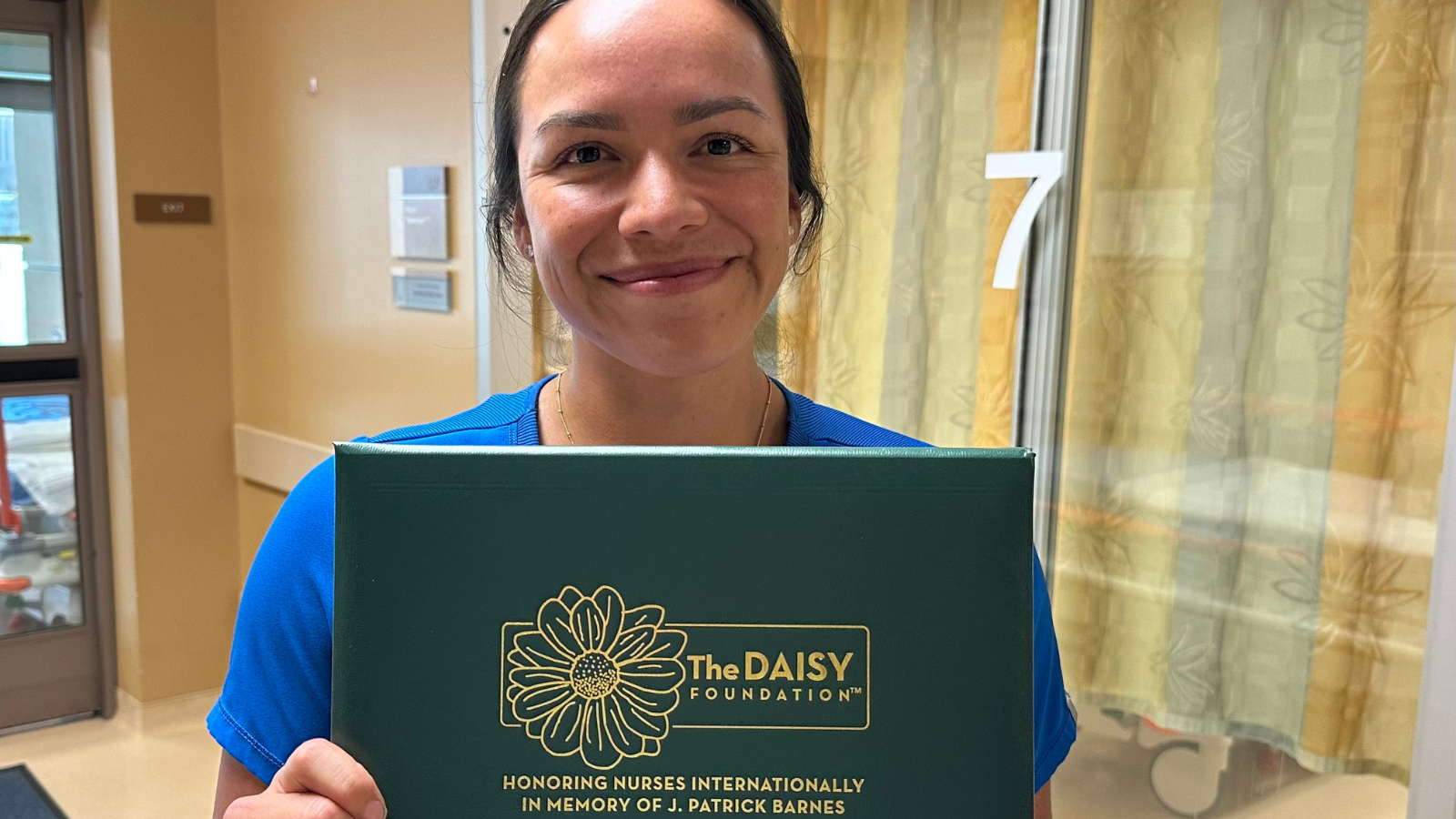 The image shows a smiling nurse holding a plaque from the DAISY Foundation, honoring nurses for their exceptional care.