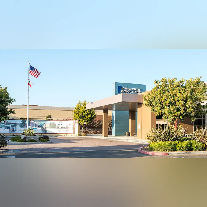 The image shows the entrance of Lompoc Valley Medical Center, featuring landscaping and American and California flags.